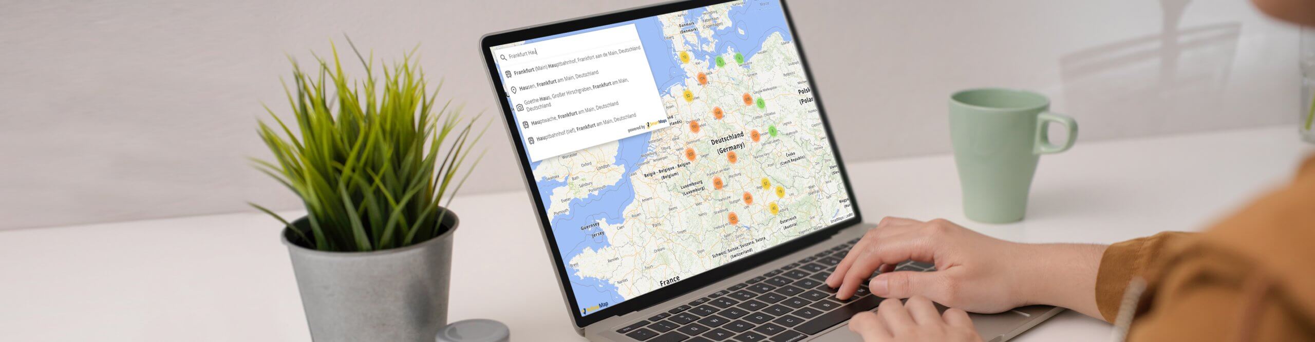 Eine Person sitzt vor einem Laptop, auf dem ein Kartenausschnitt von Deutschland zu sehen ist, und nutzt die Autocomplete-Funktion von SmartMaps für eine Adresseingabe.