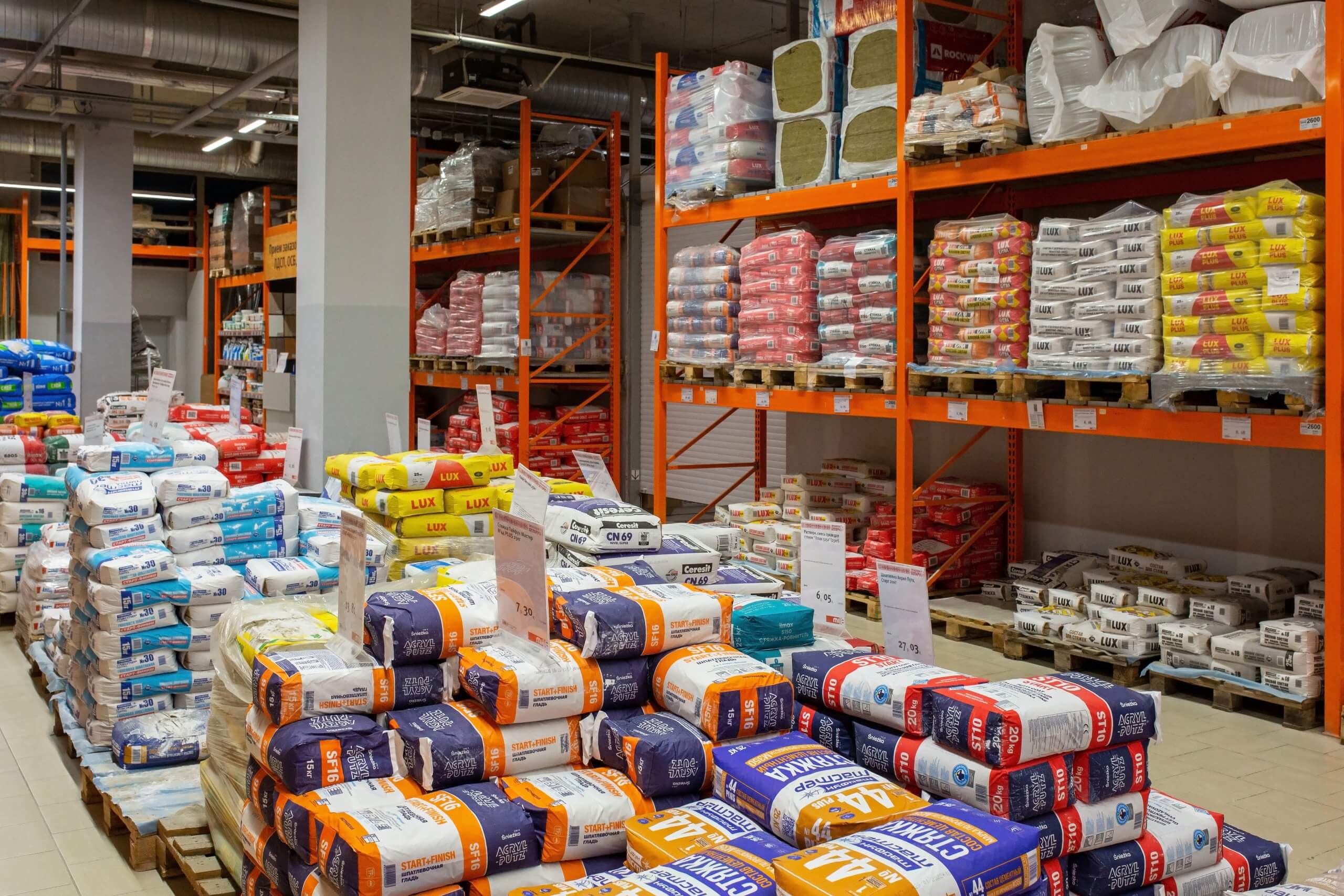 Verschiedene Baustoffe und Materialien in Regalen und auf Paletten in einem Industrielager.