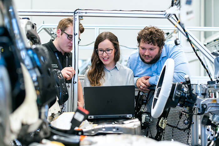 Drei Personen in einem Forschungslabor der Automobilindustrie tauschen sich aus und blicken dabei auf einen Laptop.