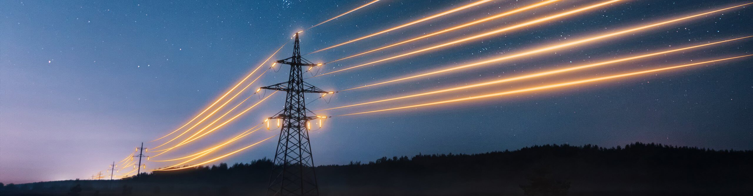 Ein Strommast mir beleuchteten Stromleitungen bei Nacht.